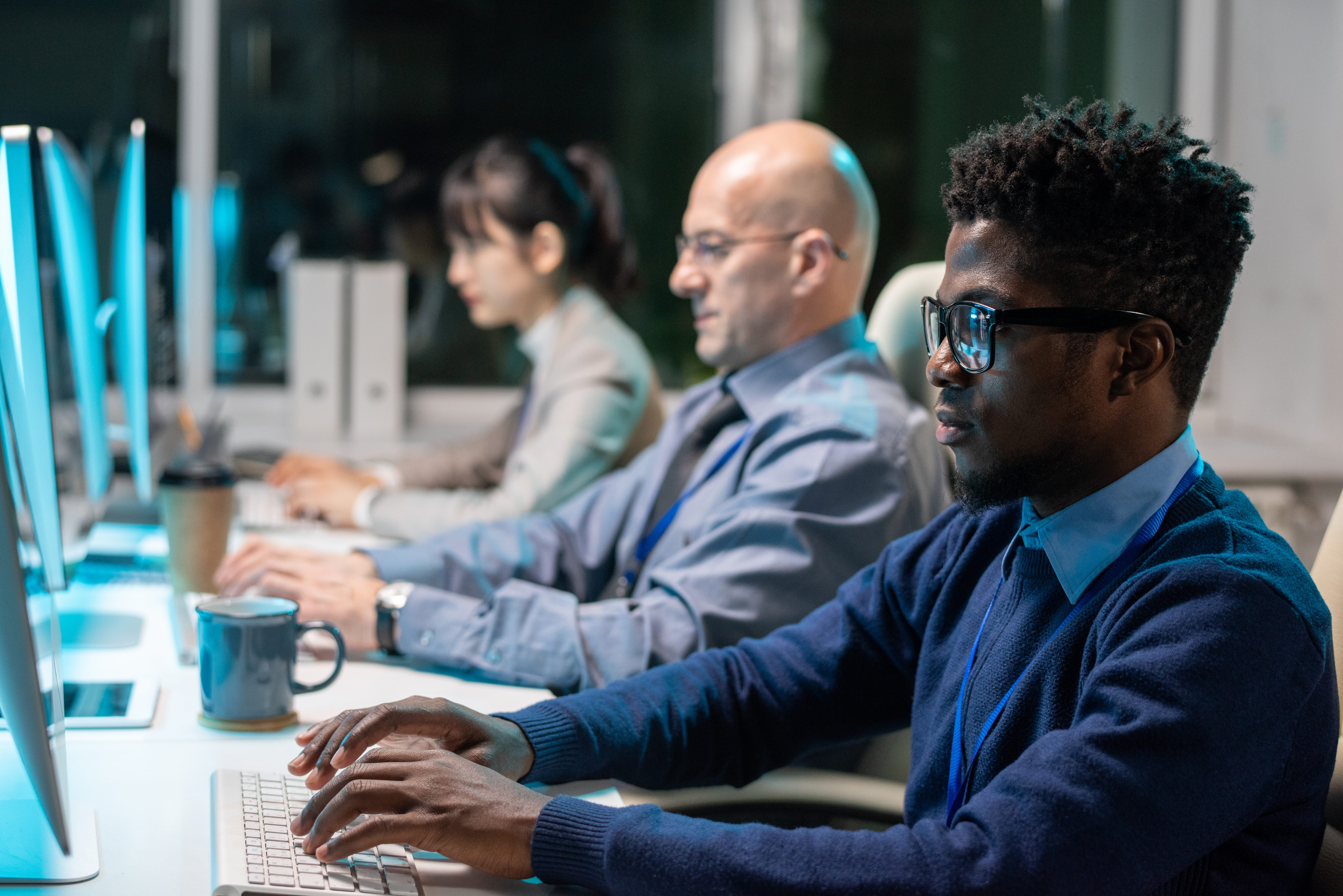 Row of contemporary intercultural programmers working over new software in front of computer monitors in office